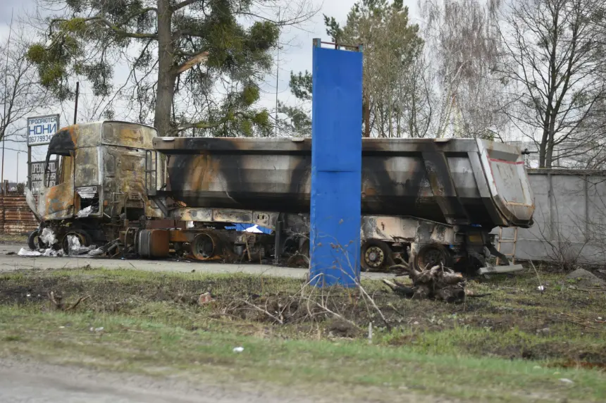 Heavily burnt dump truck wreckage lying roadside after an accident. The destroyed commercial vehicle is charred and severely damaged.