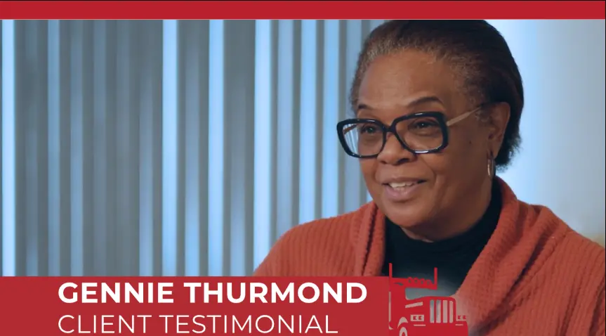 Gennie Thurmond giving a client testimonial video interview, wearing glasses and an orange sweater.