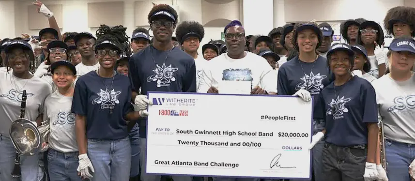 South Gwinnett High School Band winners holding a large $20,000 check after winning the Great Atlanta Band Challenge. The large group photo is taken indoors.