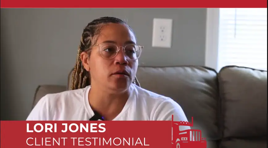 Lori Jones giving a client testimonial video interview, seated on a couch, wearing glasses and braids. 