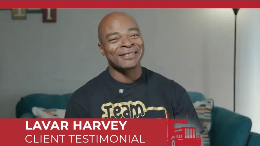 Lavar Harvey giving a smiling client testimonial video interview, wearing a dark team shirt with gold lettering. 