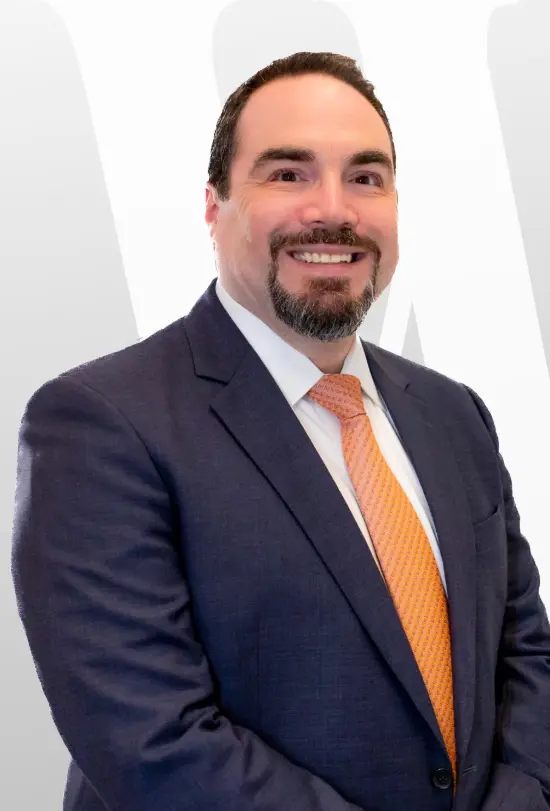 Daytime photo of several large semi-trucks, including white International and red Kenworth models, parked neatly in a row in marked spaces at a sunny truck stop.