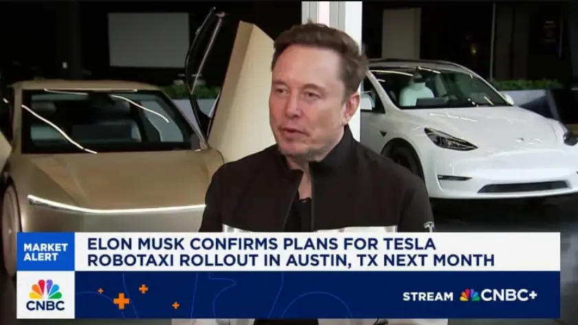 A screenshot from a CNBC segment featuring Elon Musk being interviewed in front of two Tesla vehicles (one with its gull-wing door open). A graphic banner reads: "ELON MUSK CONFIRMS PLANS FOR TESLA ROBOTAXI ROLLOUT IN AUSTIN, TX NEXT MONTH."
