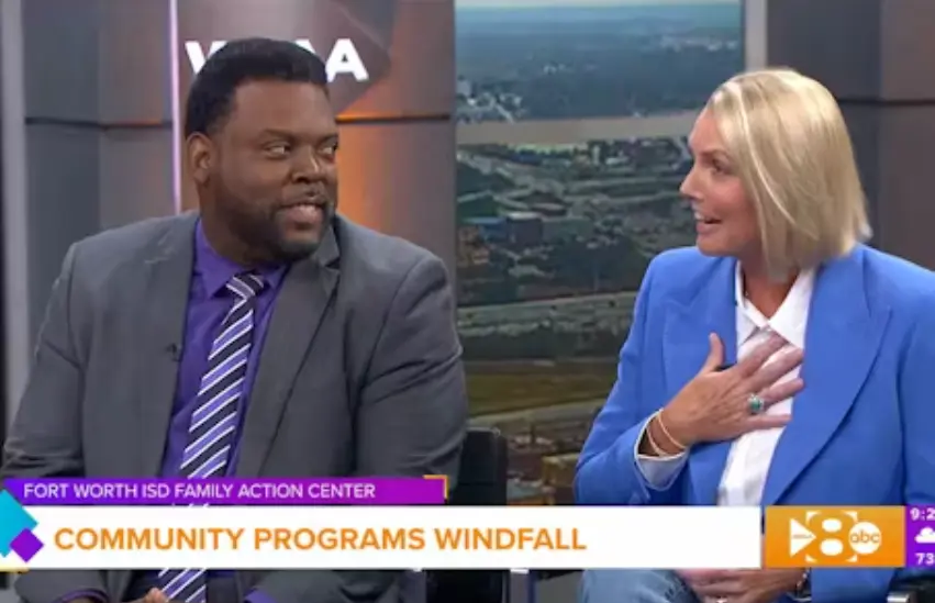 A screenshot from a news segment featuring a man in a gray suit Amy Witherite, in a bright blue blazer, talking during an interview. A graphic banner reads "FORT WORTH ISD FAMILY ACTION CENTER" and "COMMUNITY PROGRAMS WINDFALL."