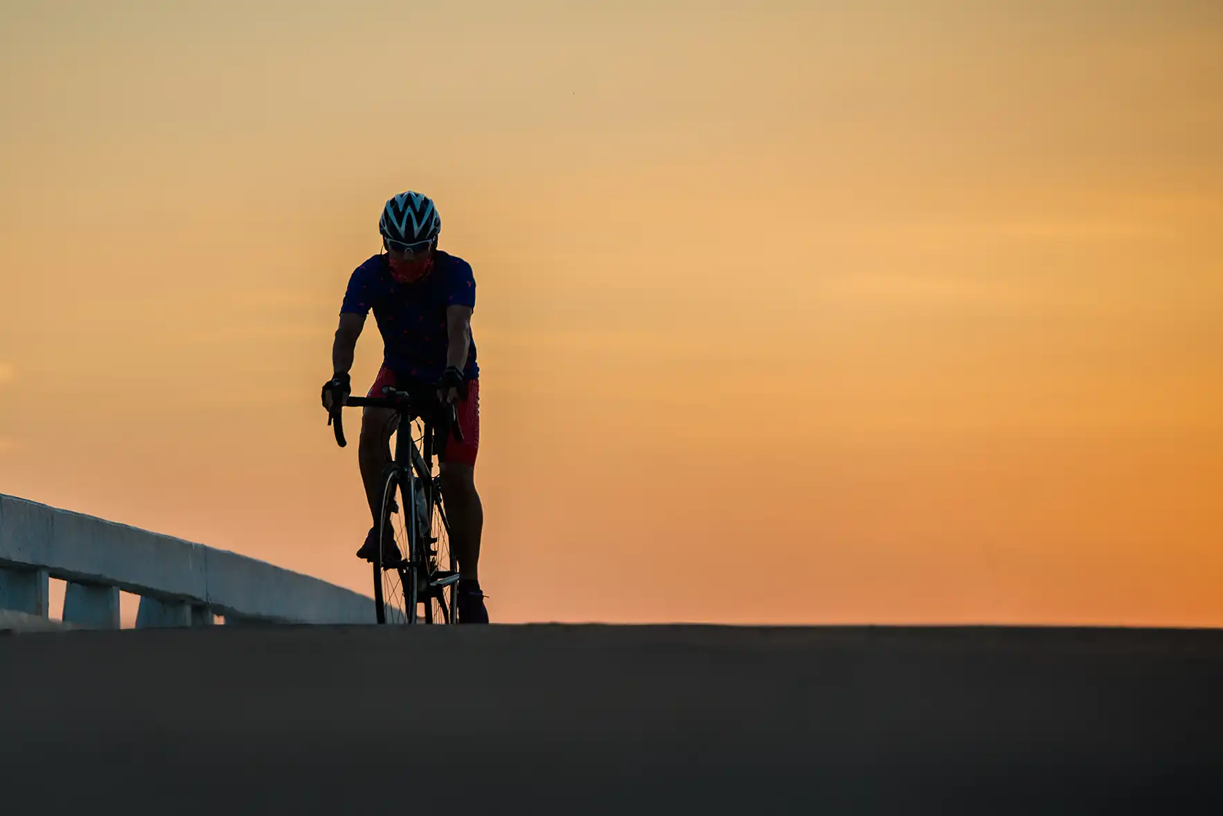 Silhouette man rides bike sunset sky background