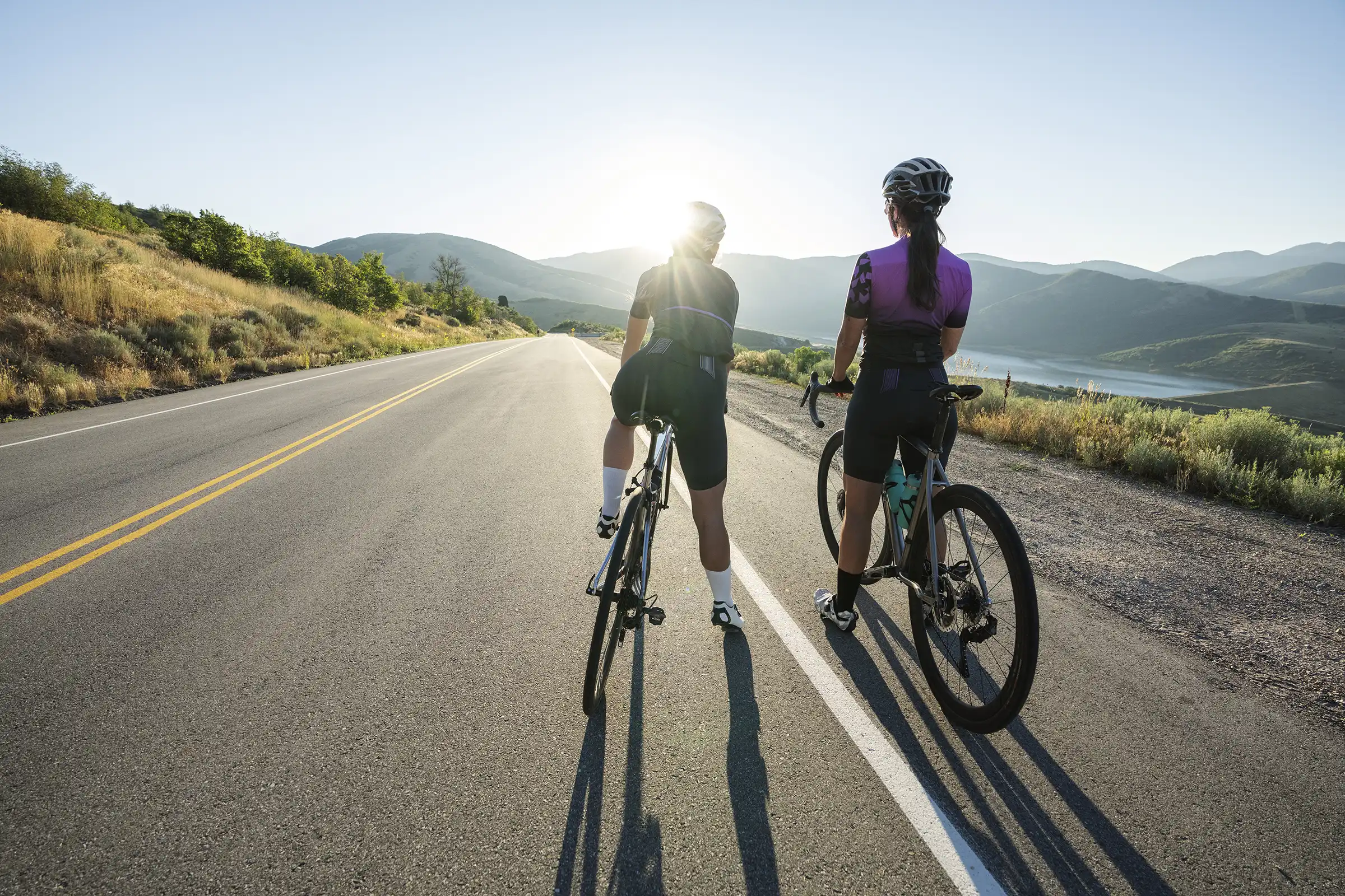 Two cyclists looking down an empty highway just after sunrise