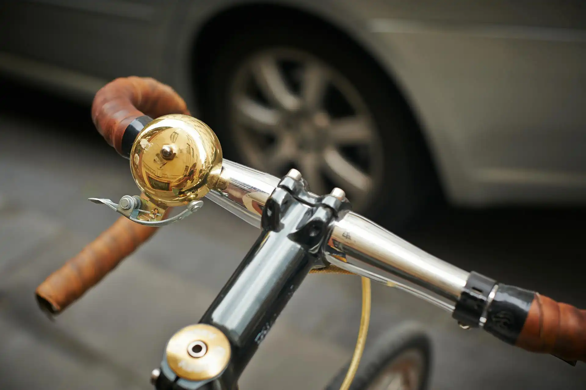 Bicycle handlebars with brass bell and car in background