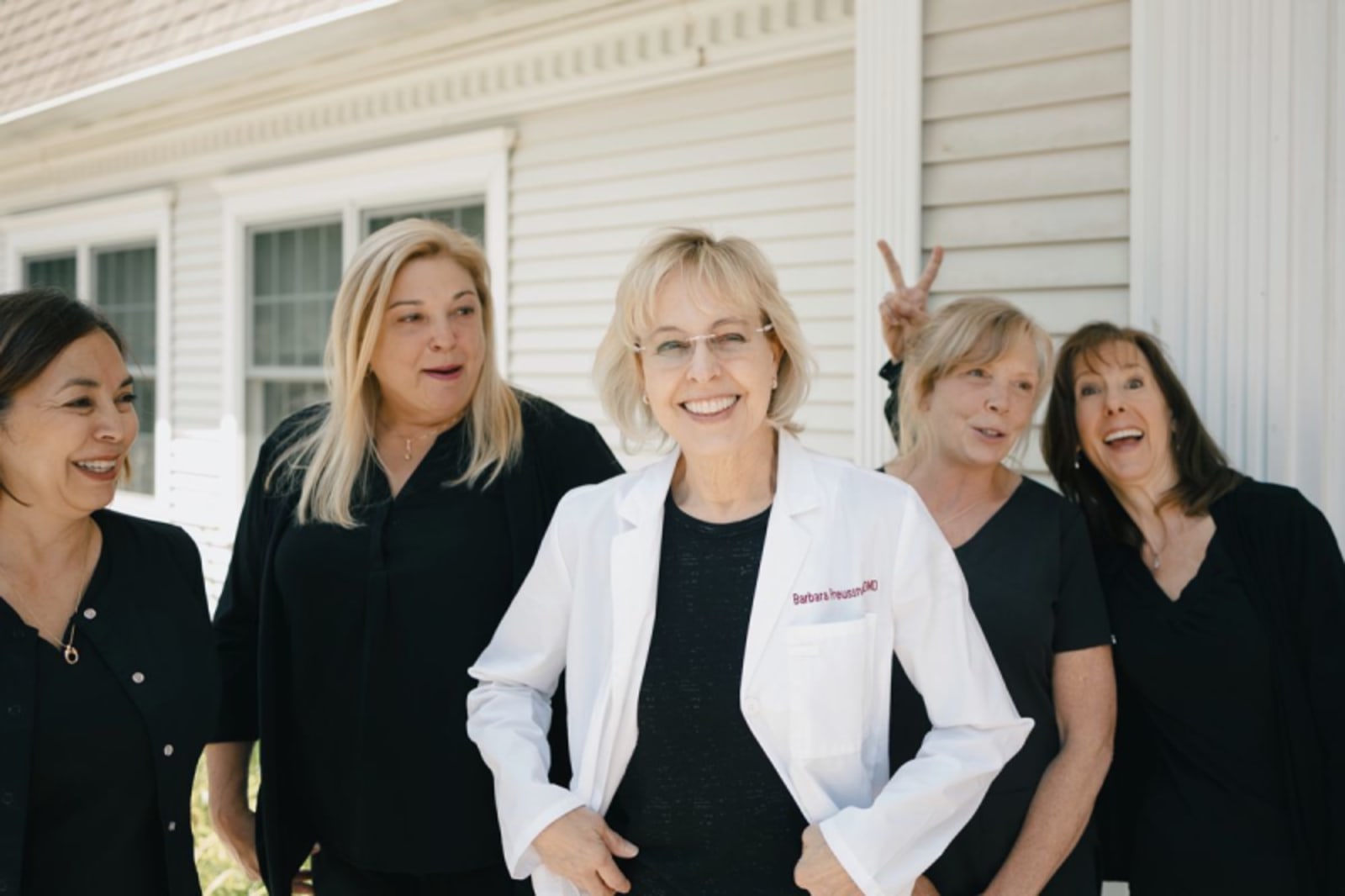 Dental team of five women in professional attire standing together outside a white building with columns.
