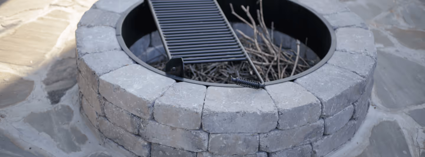 A circular outdoor fire pit with a cooking grate on a stone patio