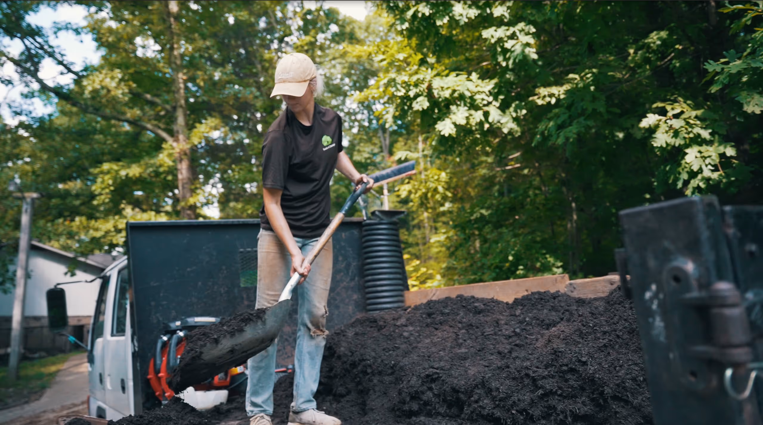 Woman shoveling dark soil near forested outdoor setting