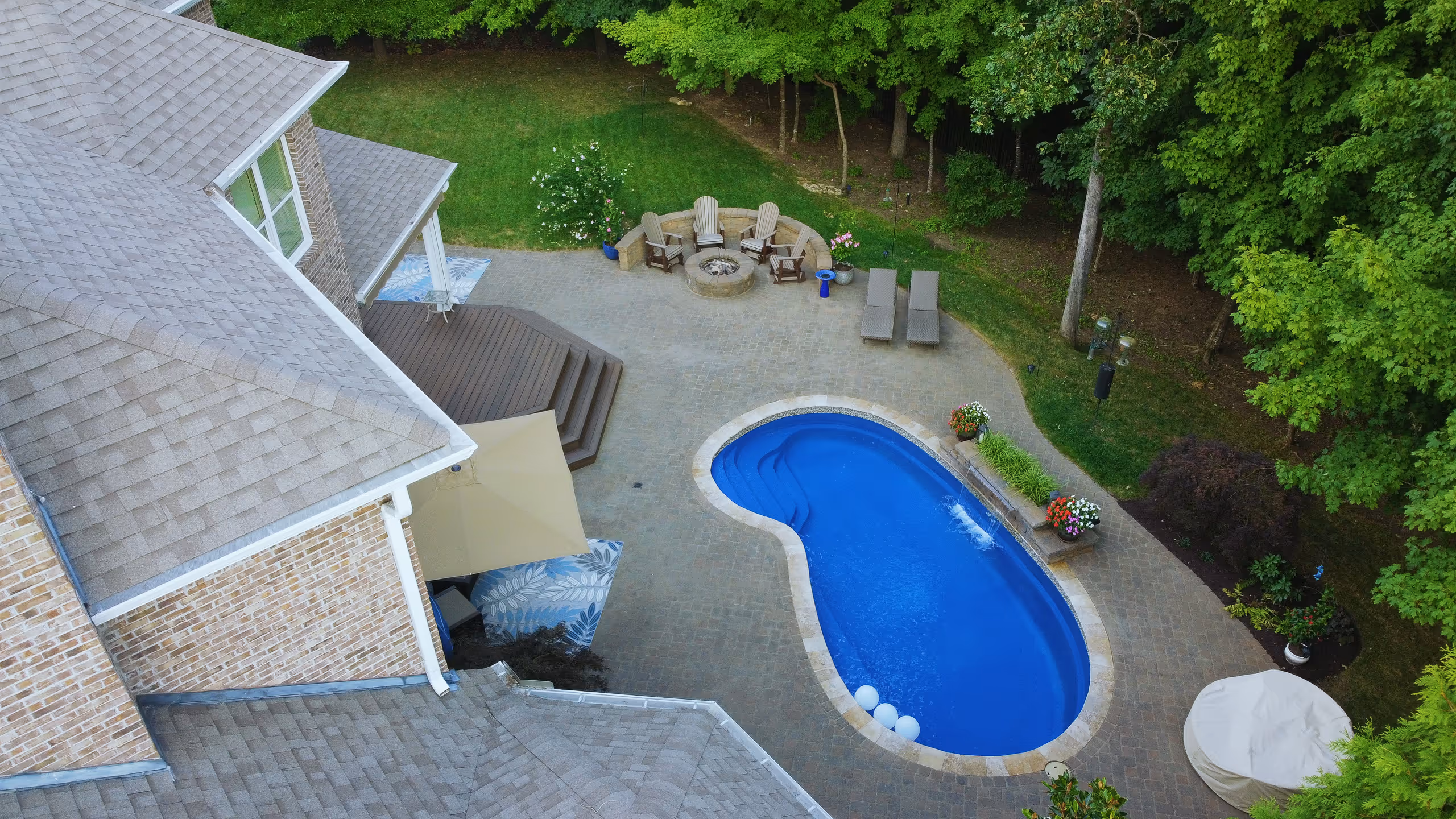 Aerial view of a backyard with a swimming pool, patio, and fire pit
