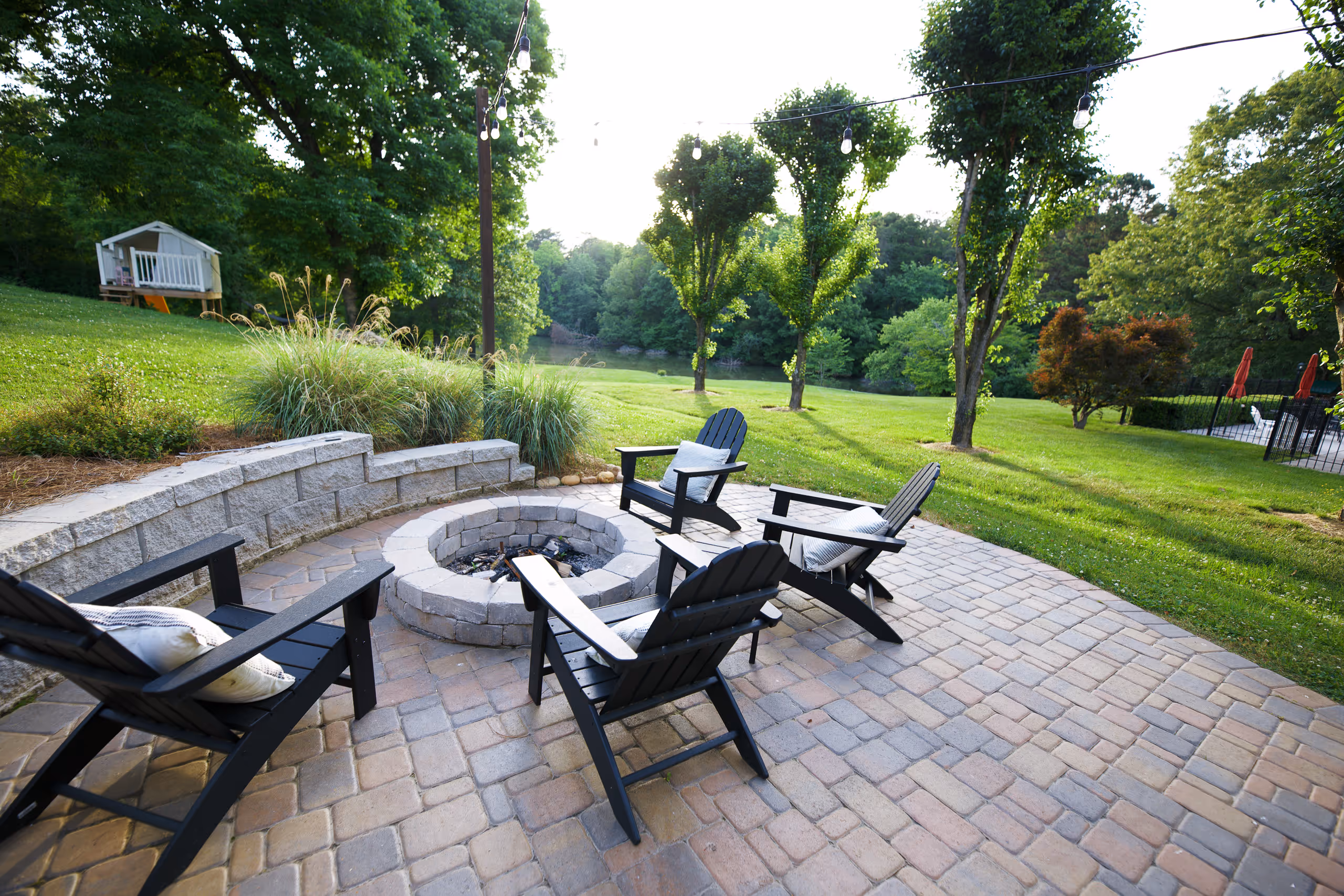 Backyard patio with a fire pit, chairs, and a view of a lush green lawn