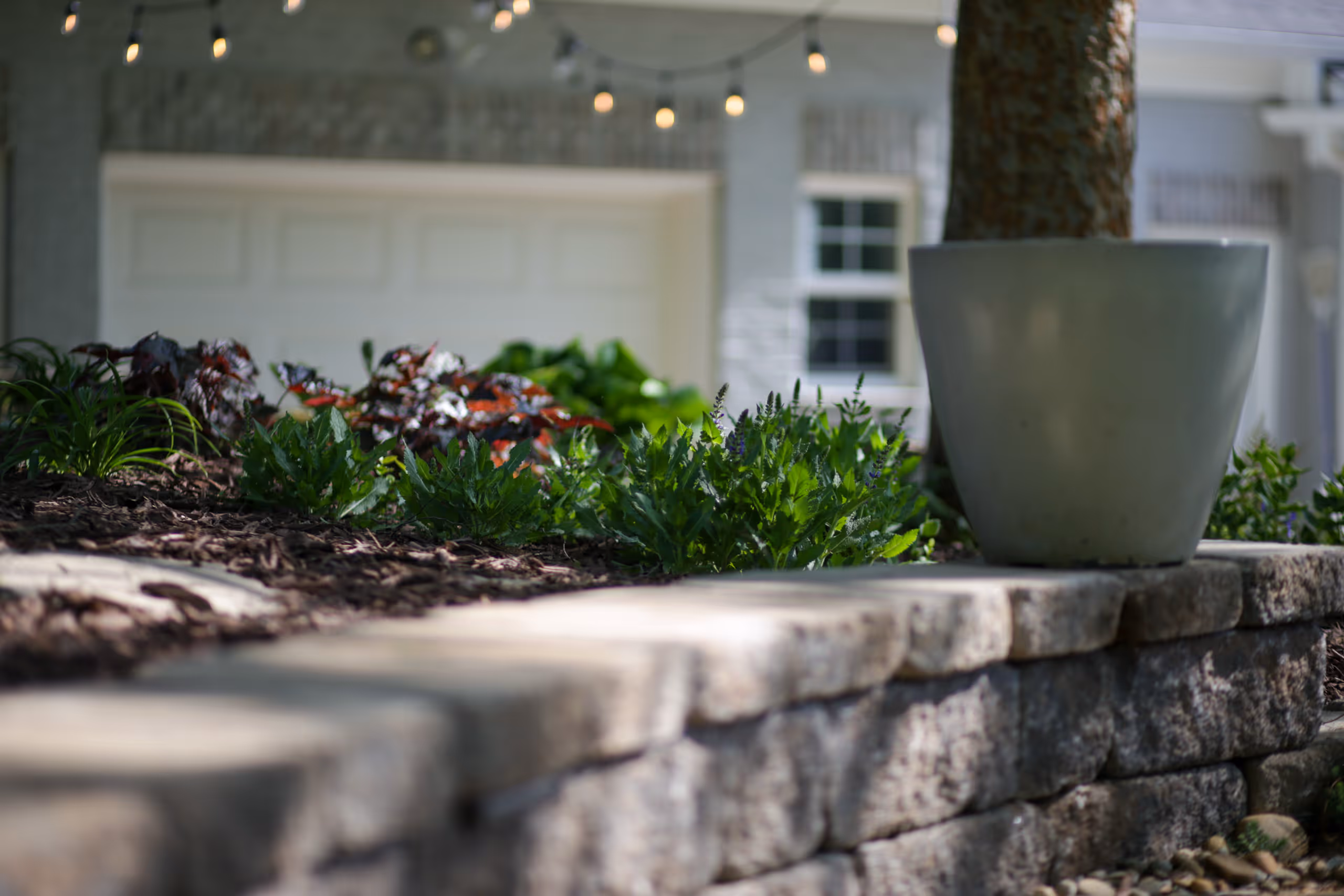 White planter on a stone wall with plants in the foreground
