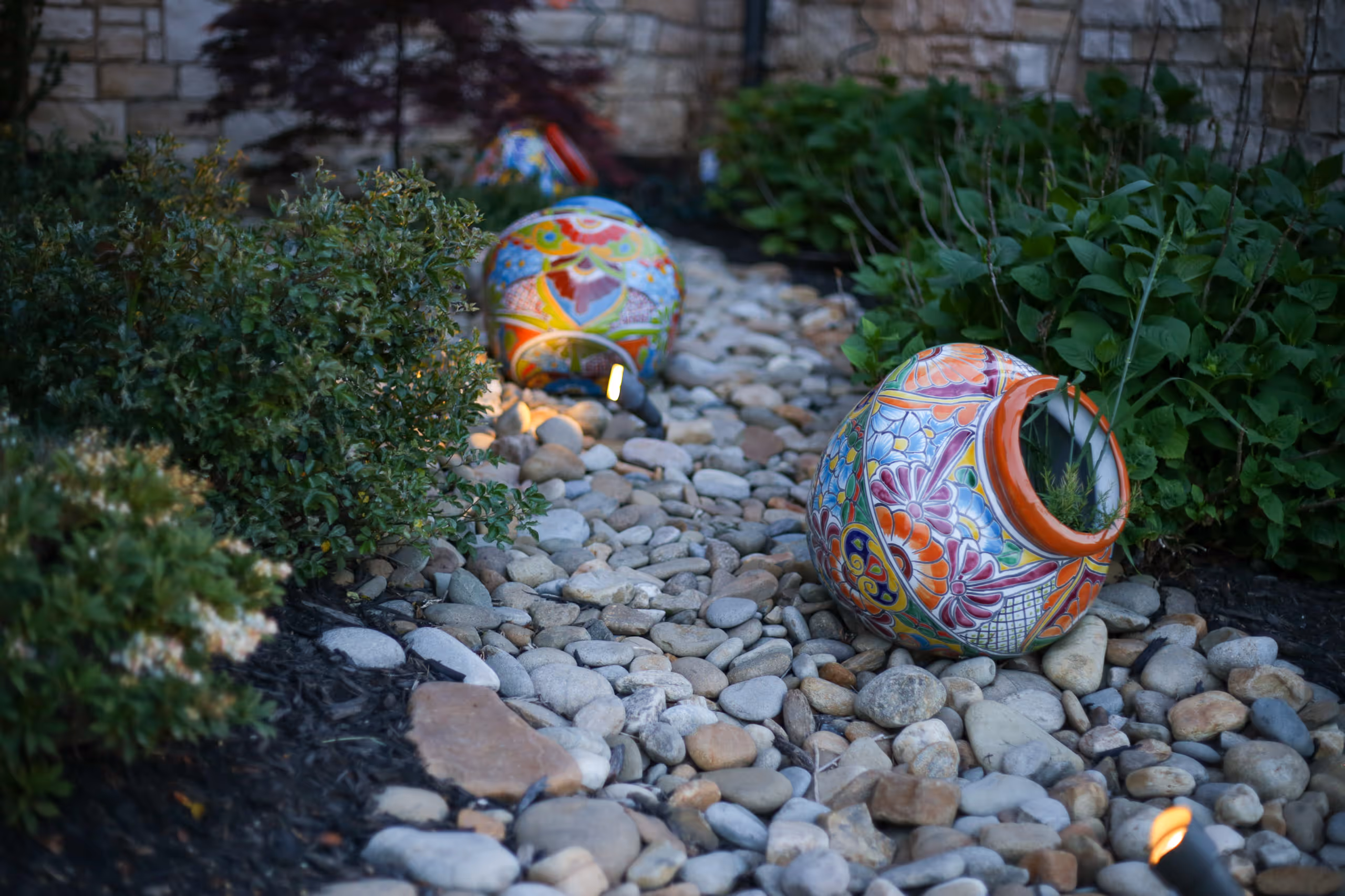 Colorful pottery jars on a bed of rocks surrounded by greenery