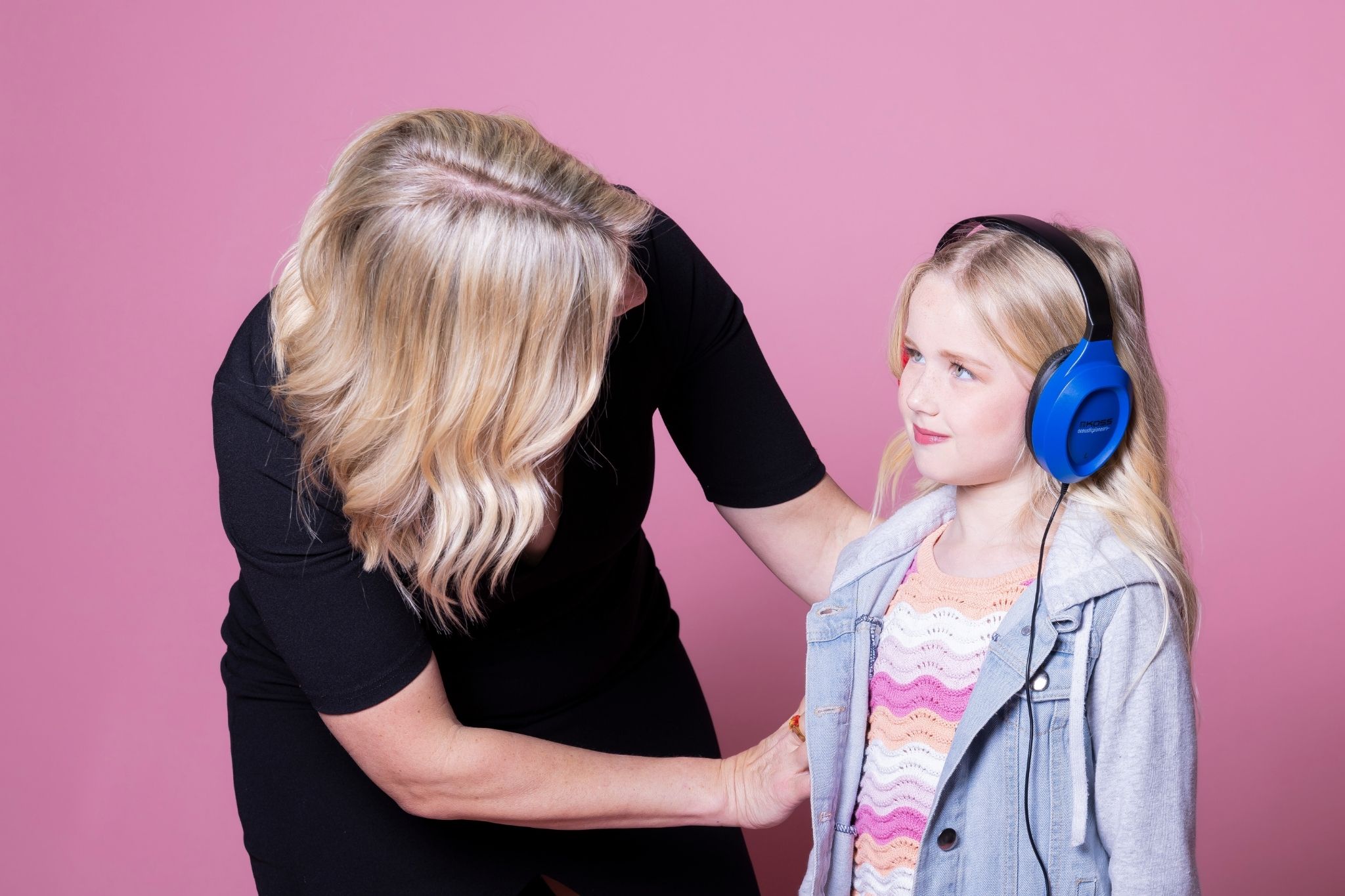 An audiologist gently places noise-canceling headphones on a young girl during a hearing evaluation for auditory processing disorder.
