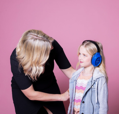 An audiologist gently places noise-canceling headphones on a young girl during a hearing evaluation for auditory processing disorder.