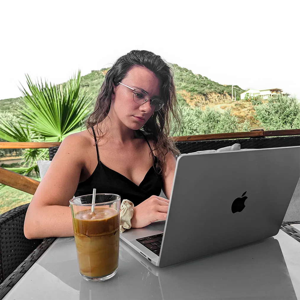 A woman working on her laptop having a frappe drink next to her.