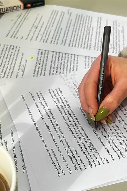 Person reviewing a manuscript, making handwritten edits with a pen on paper.