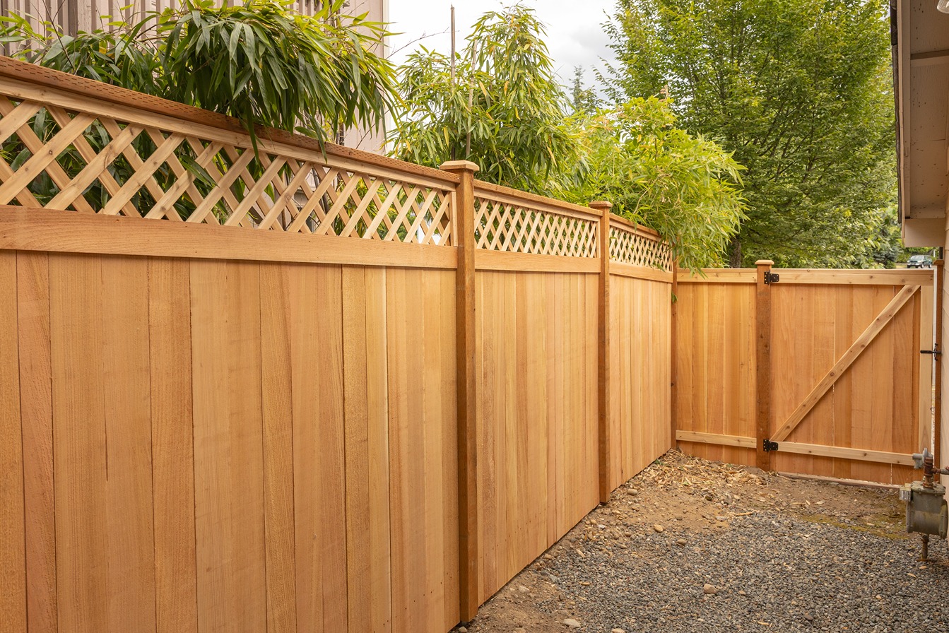  A newly constructed wooden privacy fence with a decorative lattice top section, enclosing a side yard