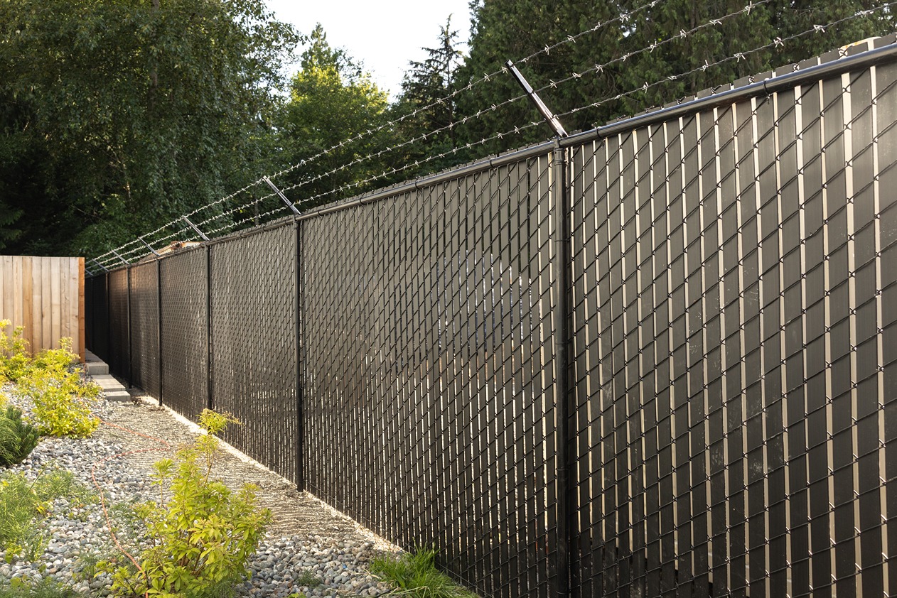 tall black chain-link fence with privacy slats and barbed wire 
