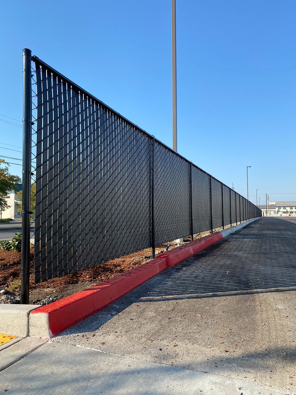 black chain-link fence with privacy slats runs alongside a newly paved road