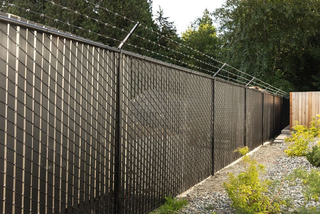 tall black chain-link fence with privacy slats and barbed wire