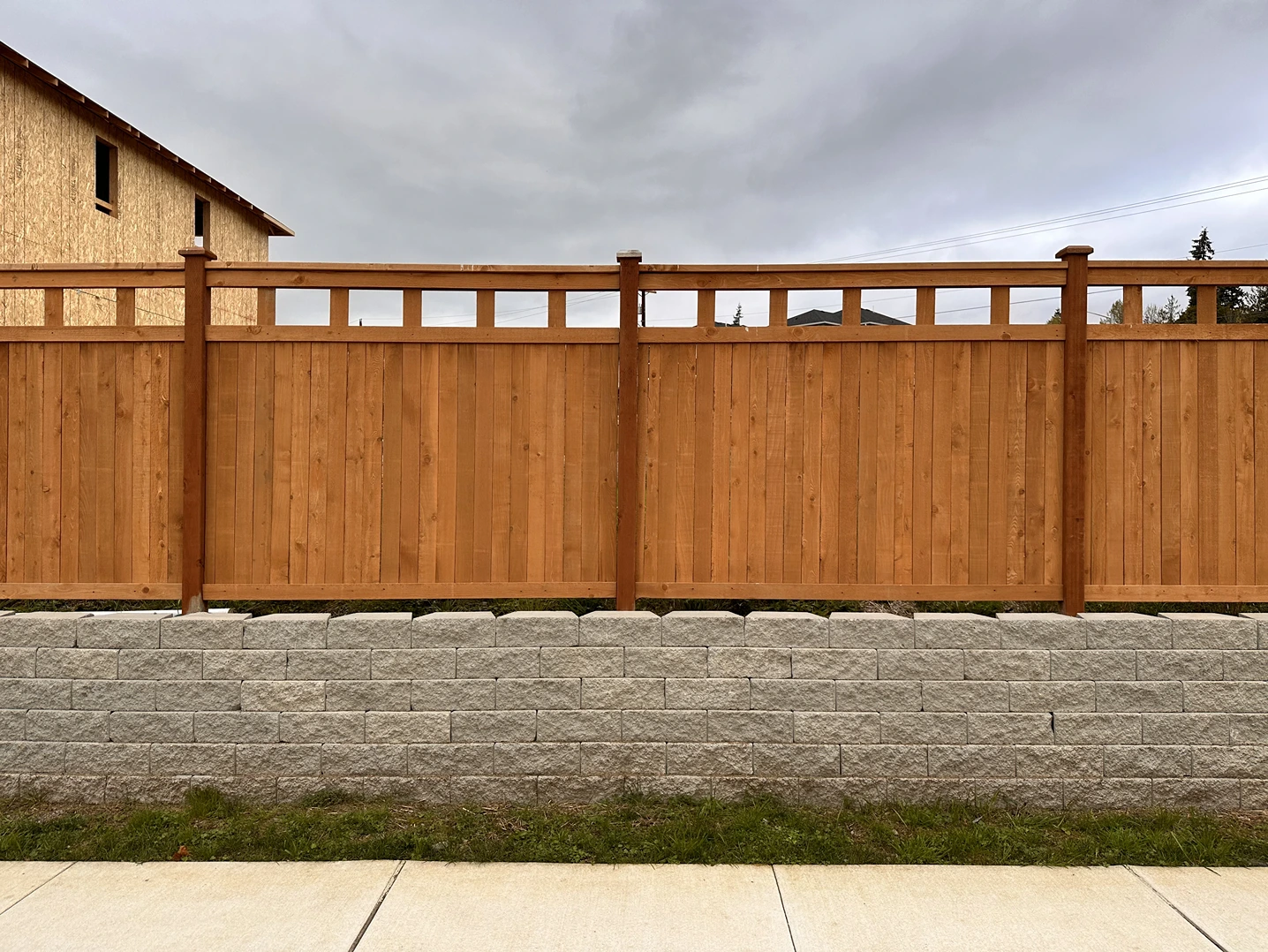 Wooden fence with a lattice top above a gray stone retaining wall under a cloudy sky.