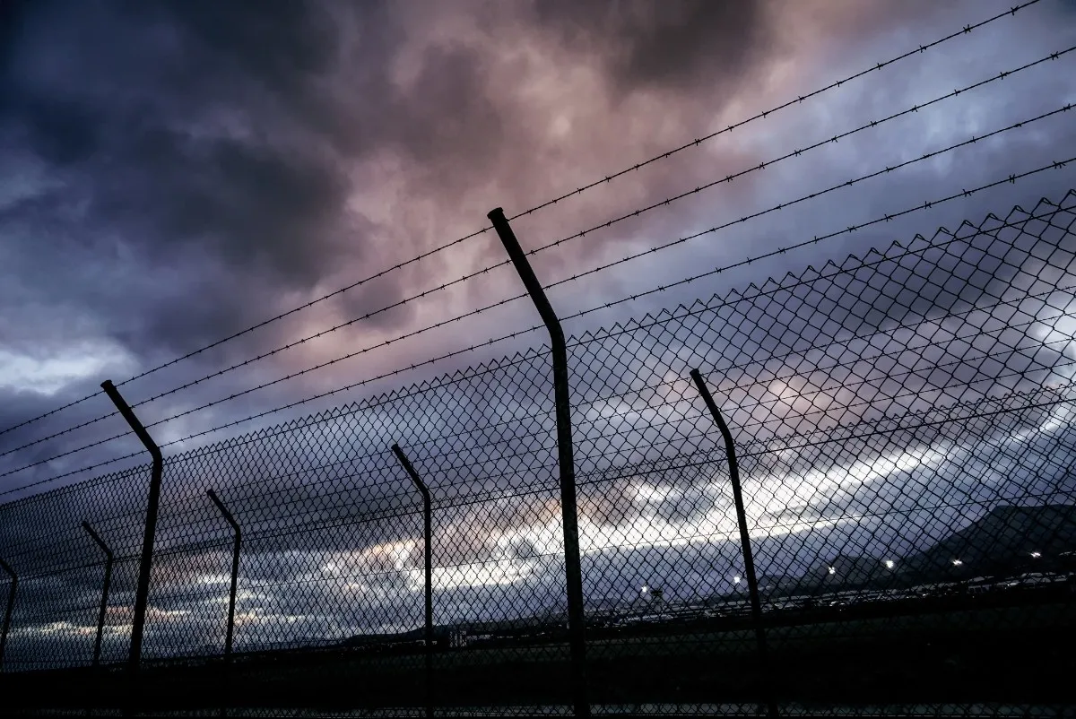 Barbed wire fence silhouetted against a cloudy, darkening sky at dusk.