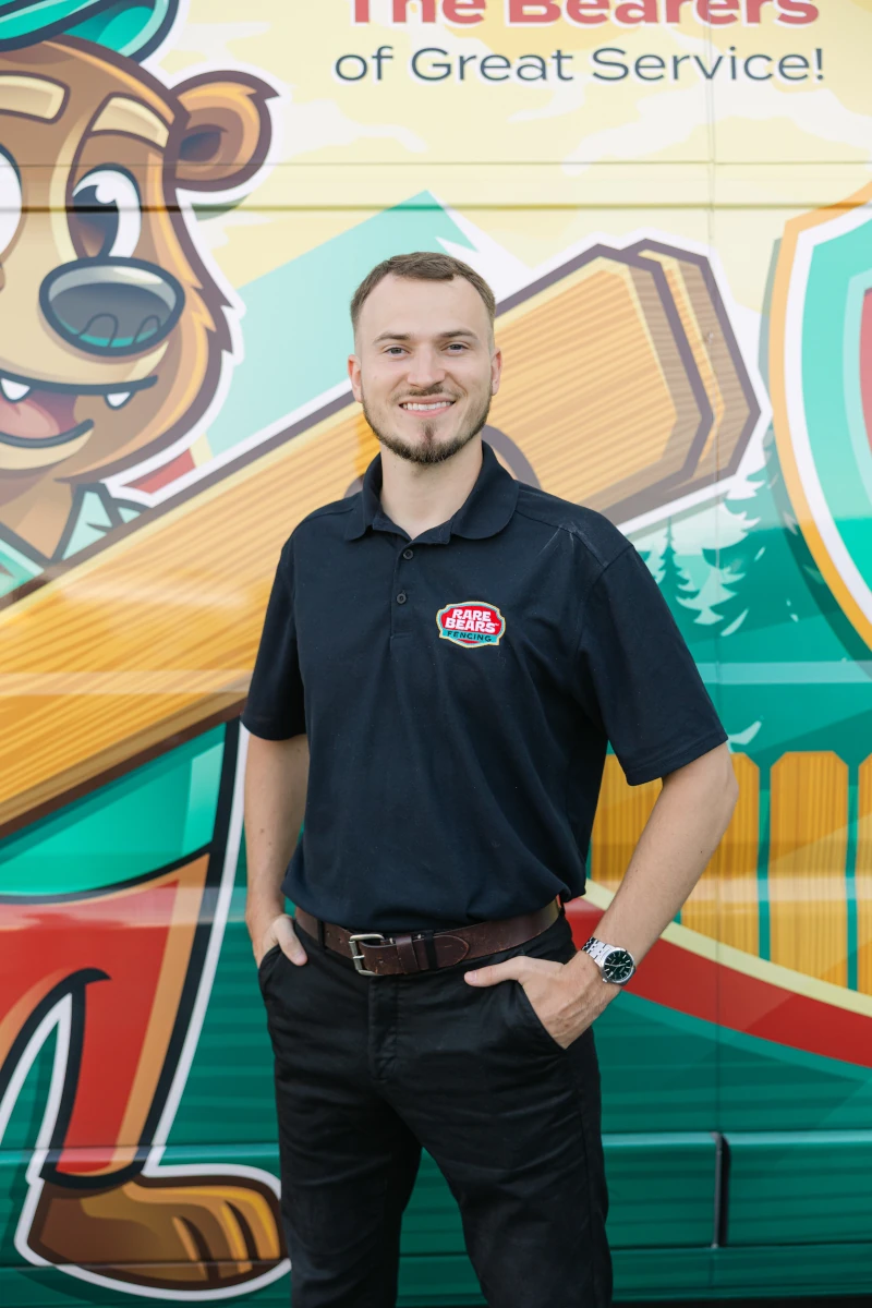 Rare Bears Fencing co-owner in a black company polo standing in front of a branded service van