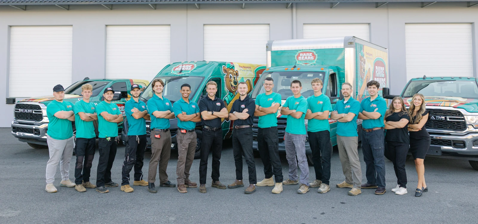 Full Rare Bears Fencing team standing in a line with arms crossed in front of the branded truck and van fleet