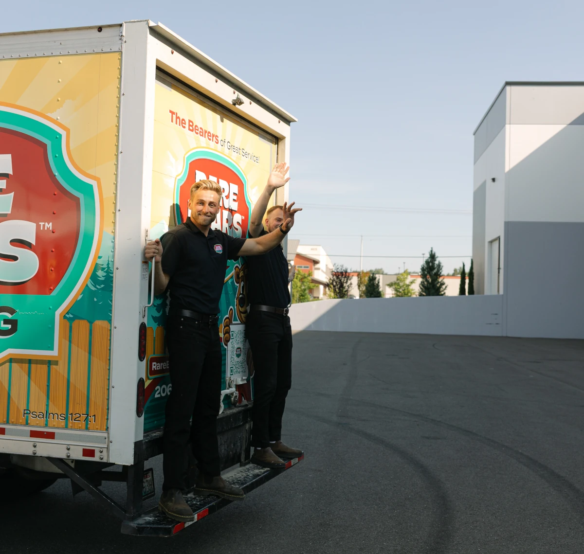 Two Rare Bears Fencing owners waving from the back of a branded box truck as it leaves the shop