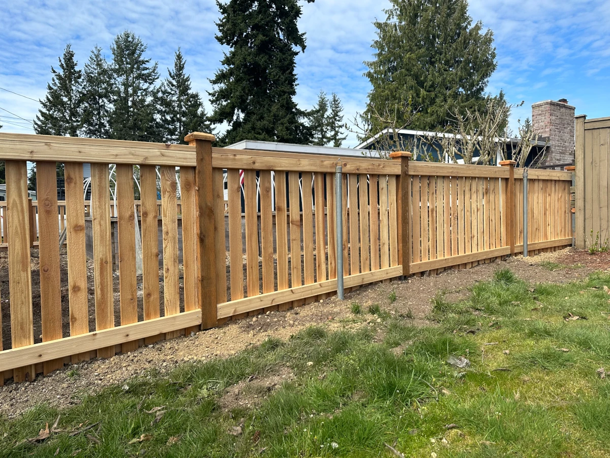 Cedar spaced-picket fence with flat top rail enclosing a backyard garden area, with evergreens behind