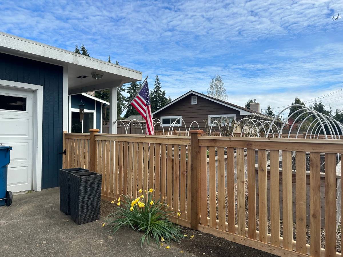 Cedar picket fence with capped posts running alongside a driveway and raised garden beds