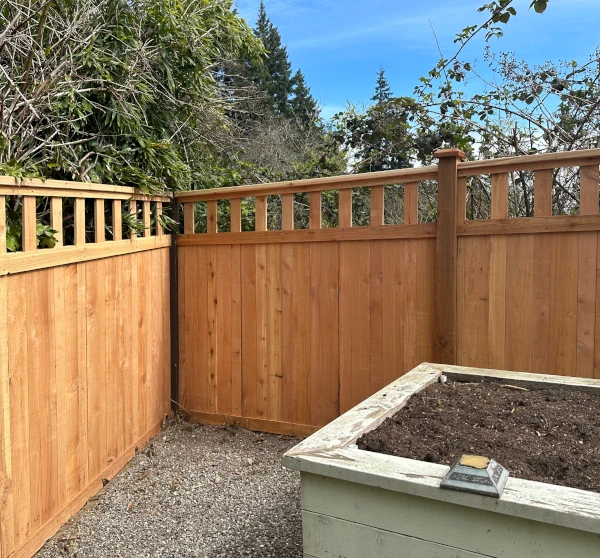 Cedar privacy fence with open square baluster top meeting at a backyard corner beside a raised garden bed
