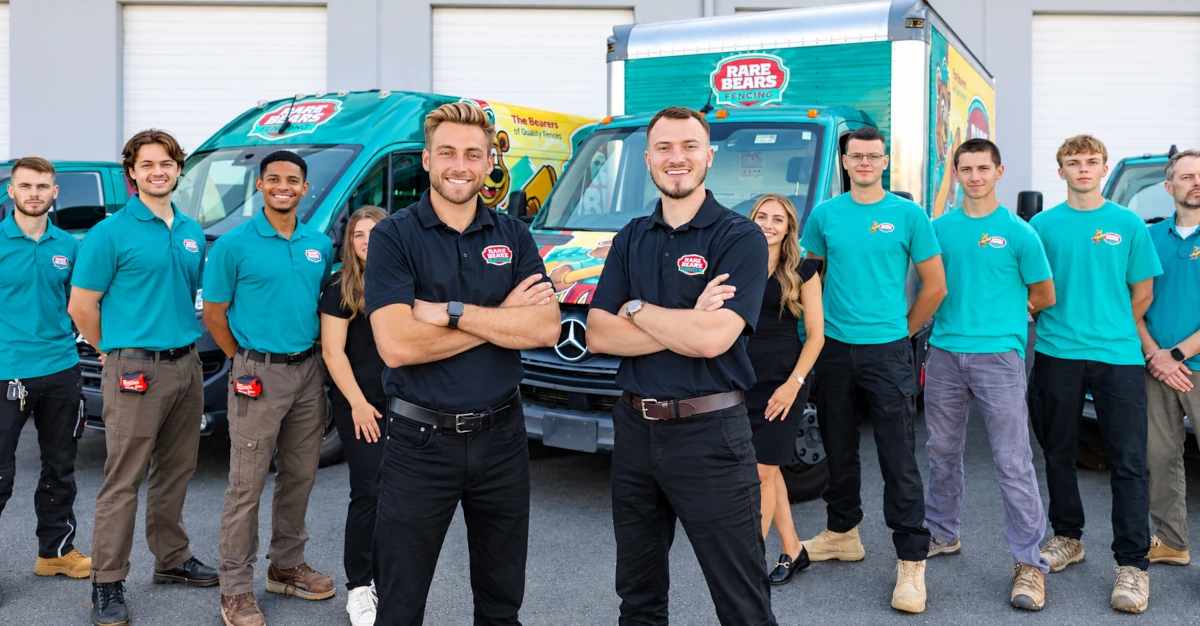 Rare Bears Fencing crew in teal uniforms posed in a V formation with two team leads in front, backed by branded vans and a box truck at the shop
