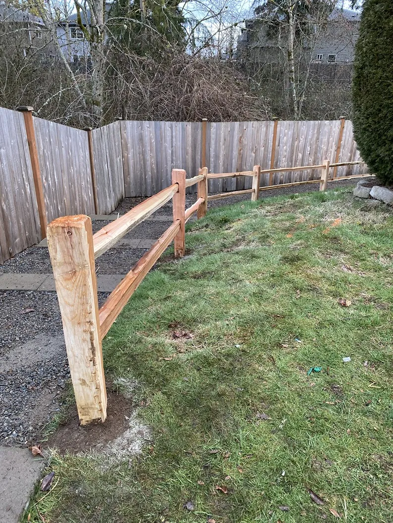 Rail wood fence with two rails and concrete-set posts marking a residential property boundary