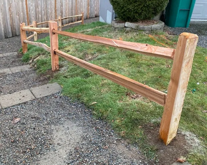 Split cedar two-rail fence with chamfered posts running alongside a gravel walkway