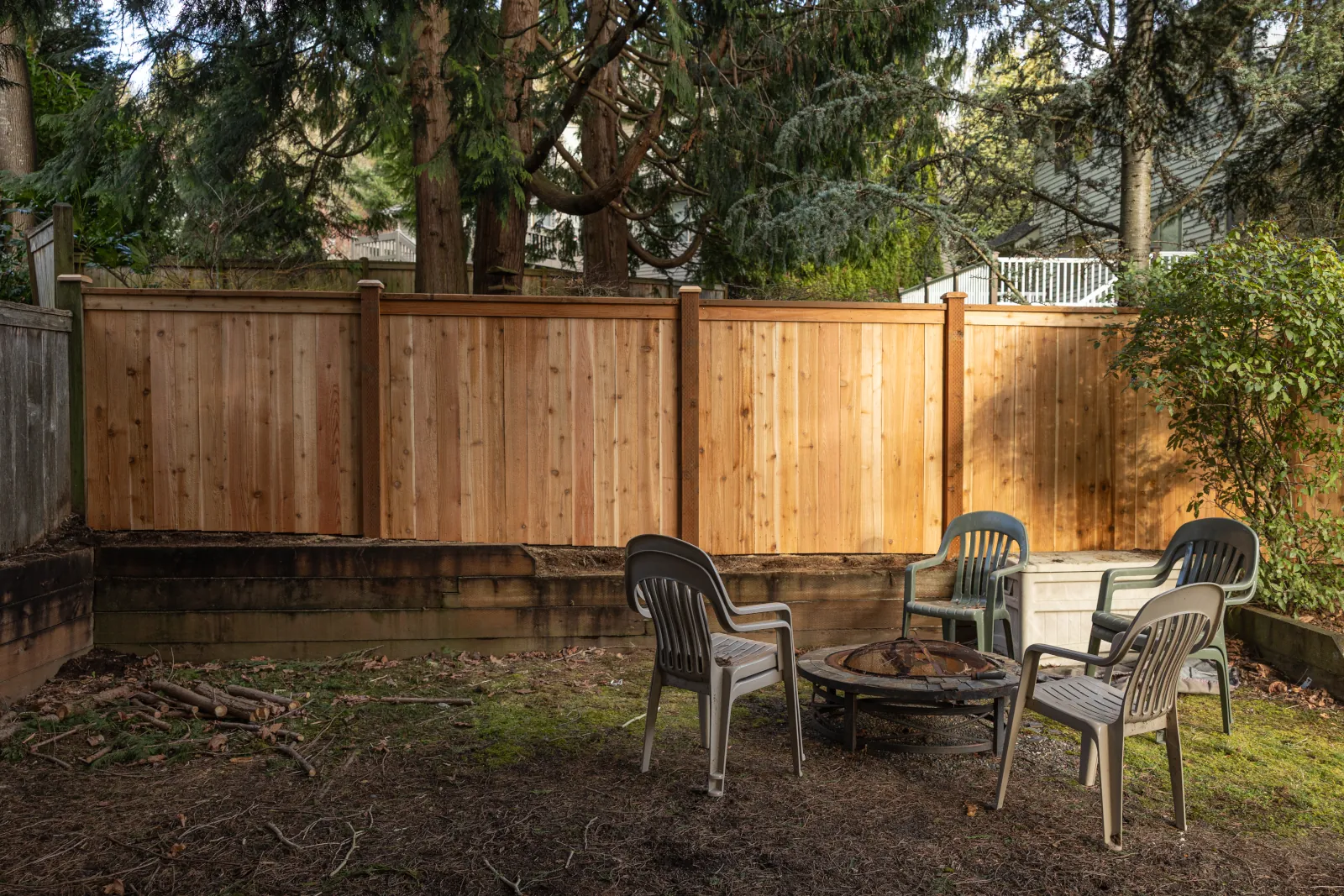 New cedar privacy fence behind a fire pit seating area in a wooded yard
