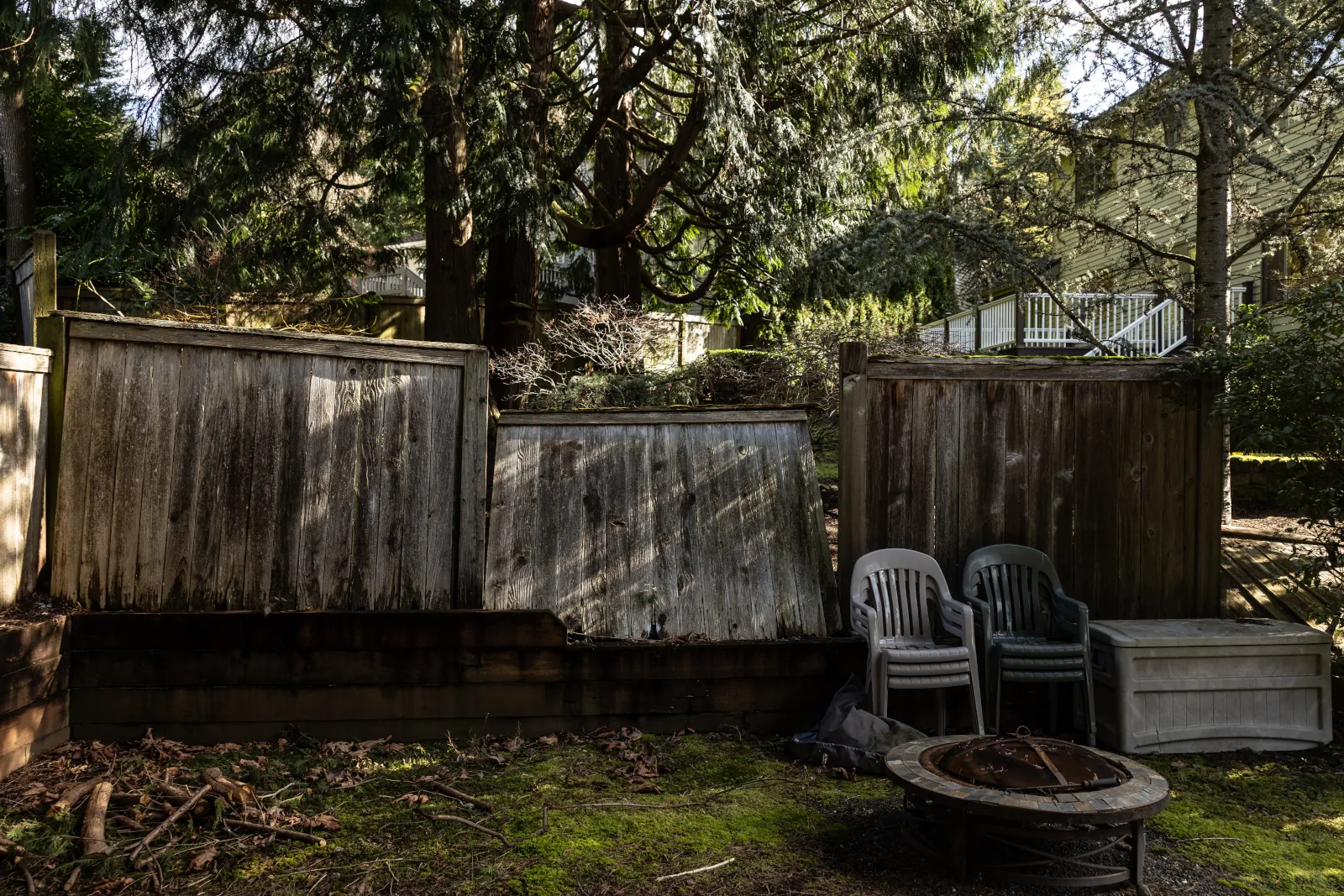 Collapsing wood fence panels leaning apart at the back of a wooded yard