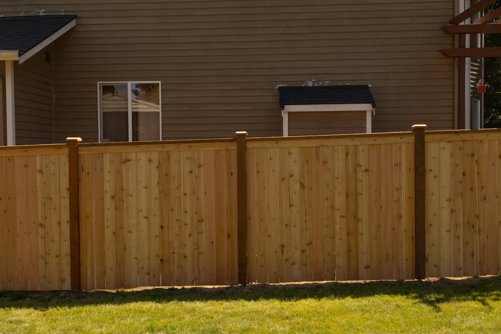 New cedar privacy fence with post caps running along a tan two-story house