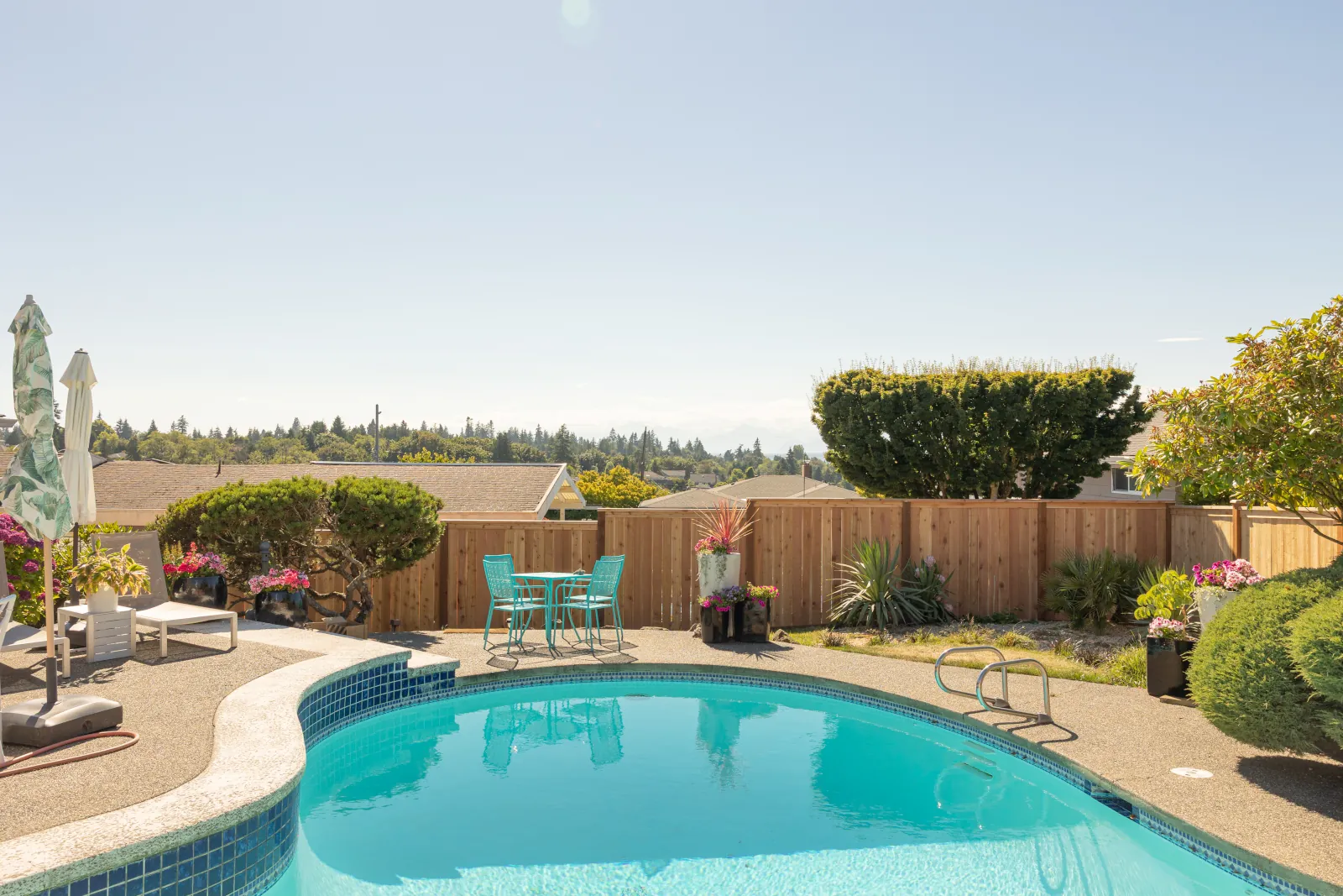 New cedar fence enclosing a hillside pool patio with teal bistro seating