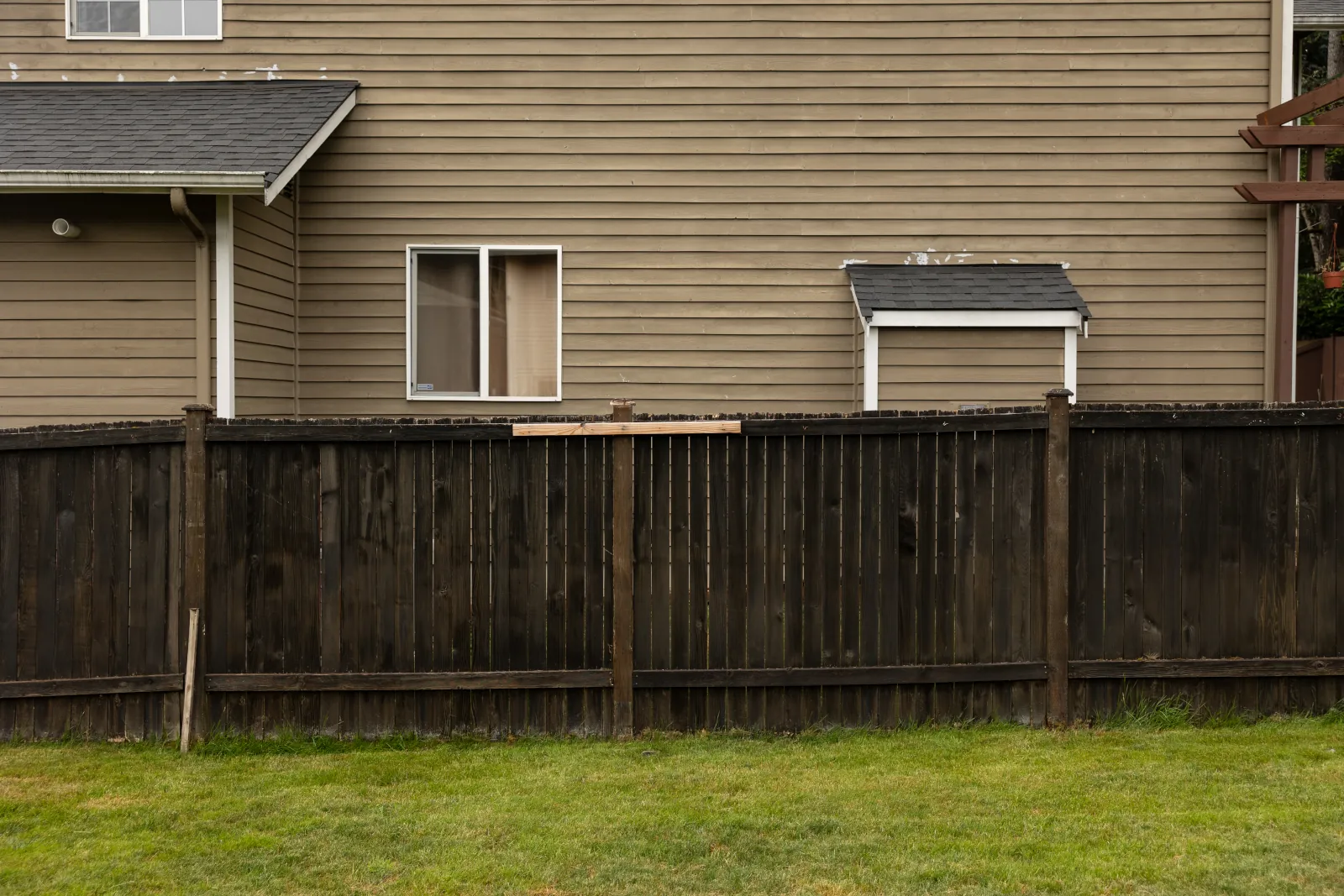 Dark stained fence with warped boards running along a tan two-story house