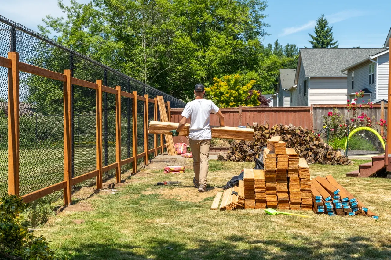 A contractor working during cedar fence installation in a suburban neighborhood