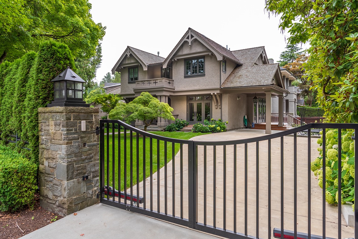 Automated black metal swing driveway gate with stone pillar