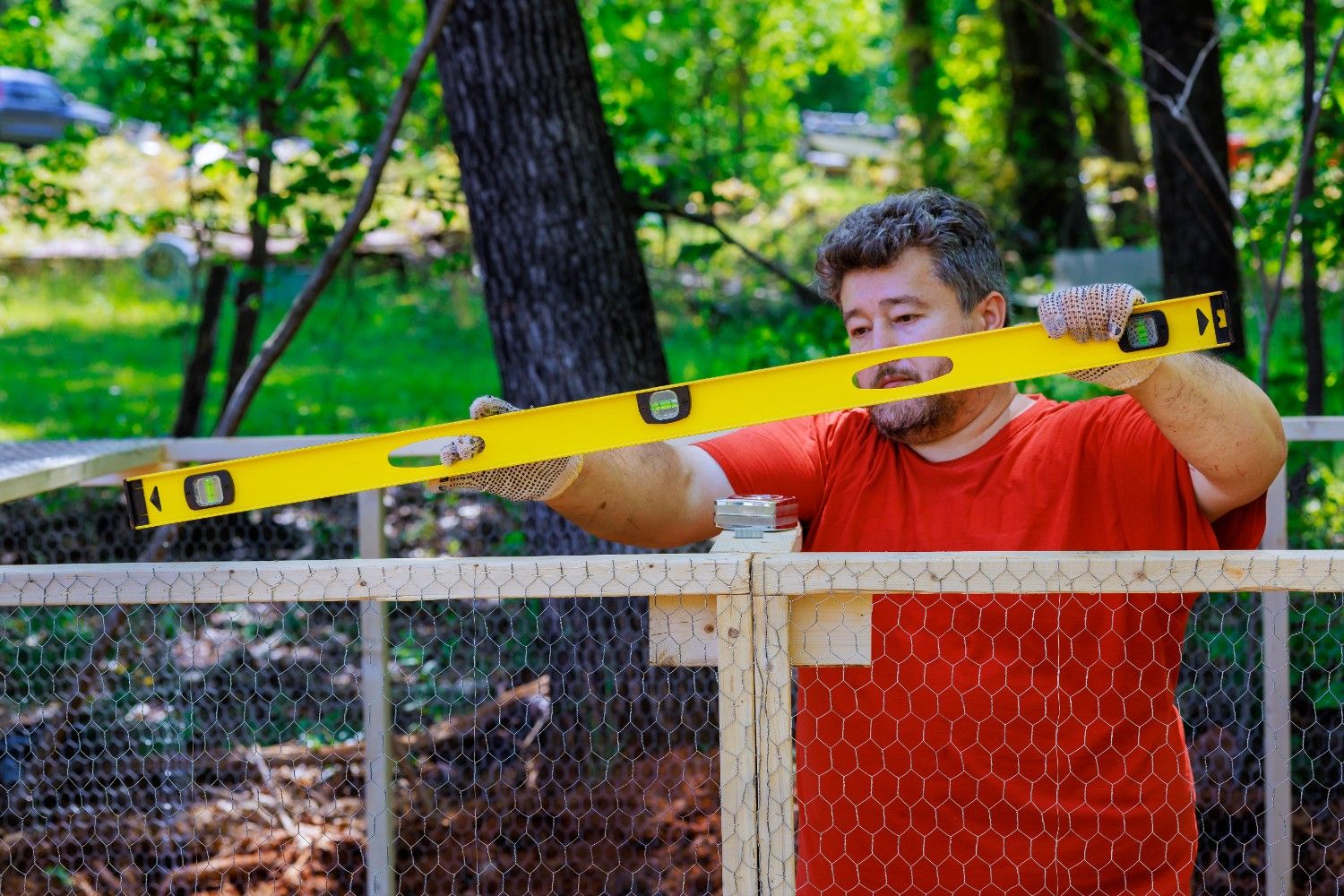 Contractor leveling a wood-framed wire fence panel during installation