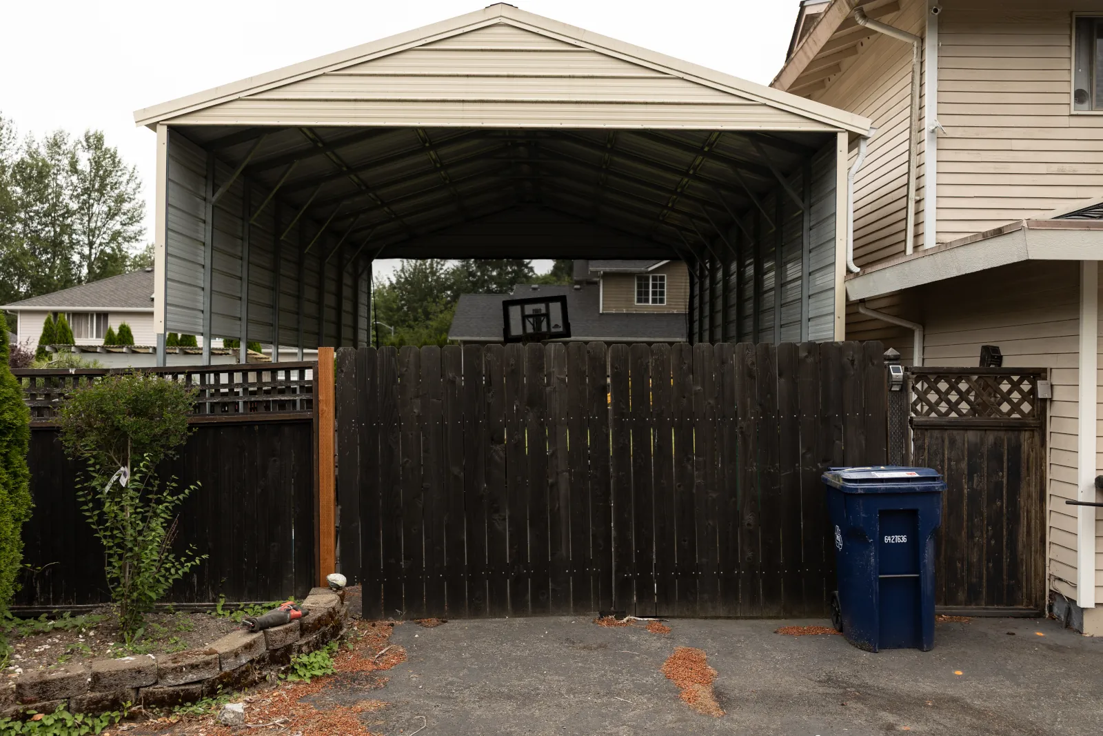 Dark stained dog-ear fence and worn double driveway gate in front of a metal carport