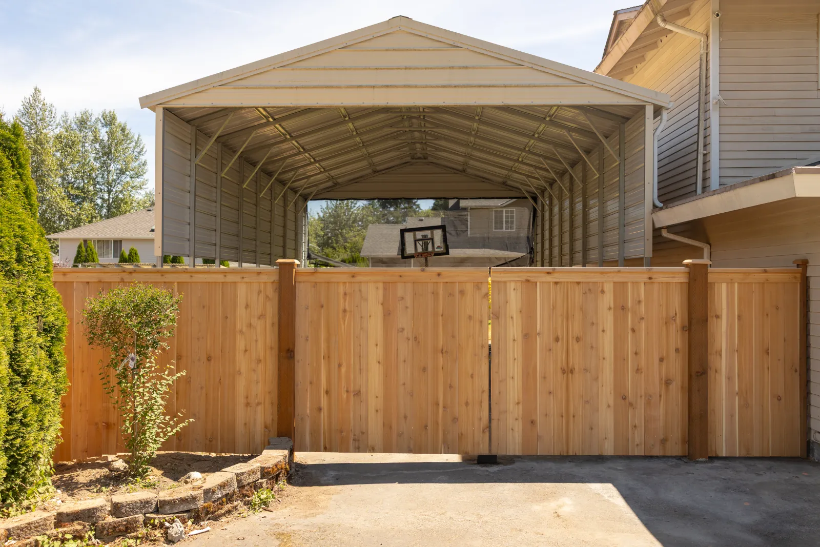 New cedar double driveway gate and privacy fence in front of a metal carport