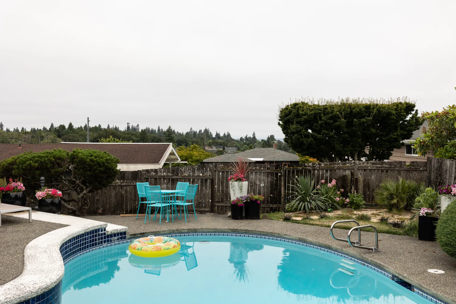 Old gray fence enclosing a hillside pool patio with teal bistro seating