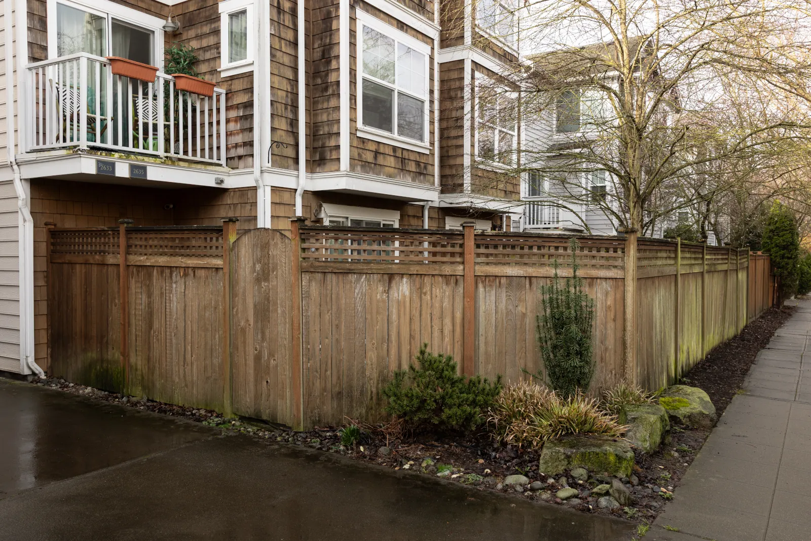 Aging wood fence with lattice top and arched gate wrapping a townhome yard