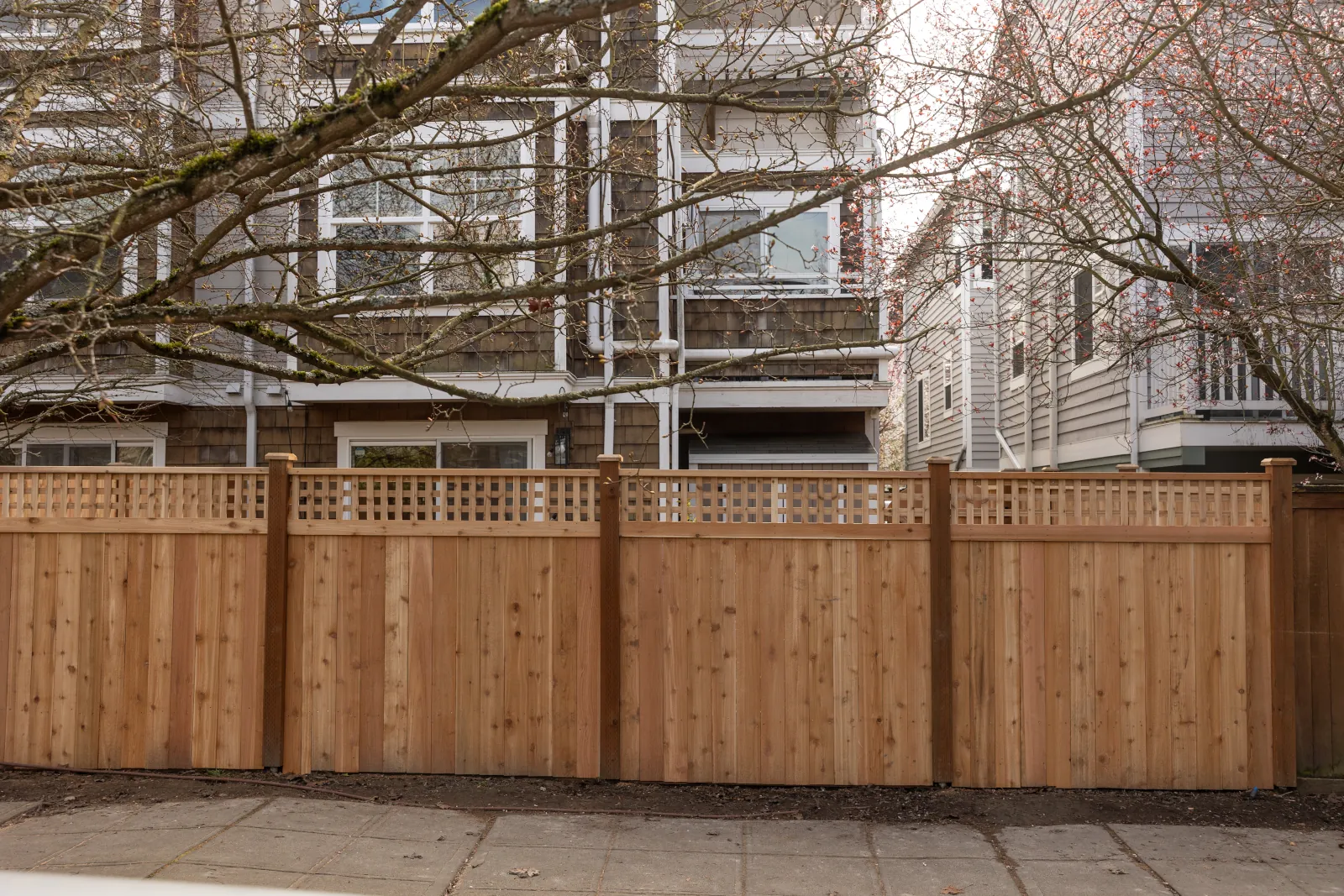 Old moss-covered wood fence with lattice top on a city sidewalk beside townhomes